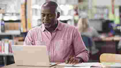 Online student adult studying social science on laptop in library